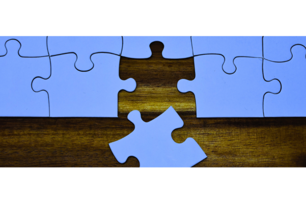 Banner image of a blank puzzle with one piece sticking out, symbolizing the missing piece needed to complete the picture or solve a problem.